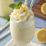 A close-up of a frosty glass from our whipped lemonade recipe, topped with whipped cream, a lemon slice, and mint.