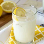 A close-up of a glass of frothy creamy lemonade with ice, garnished with a lemon wheel. This refreshing Brazilian lemonade looks delicious.