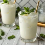 A delicious Coconut Creamy Lemonade in a sugar-rimmed glass, garnished with fresh mint on a marble counter.