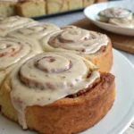 Top-down view of freshly baked banana bread cinnamon rolls generously topped with creamy cinnamon frosting in a pan.