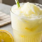A close-up of a frosty glass of delicious iced creamy lemonade, garnished with a fresh lemon slice and a sprig of mint.