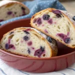 Sliced lemon blueberry sourdough bread showing airy crumb, blueberries, and lemon zest in a baking dish.