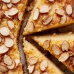 Top-down view of a golden brown lemon ricotta cake with almond flour, topped with sliced almonds