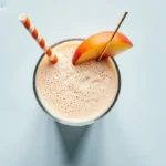 Top-down view of a creamy peach smoothie garnished with a peach slice and striped straw. Perfect peach smoothie recipe.