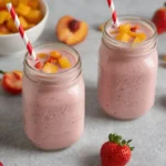 Close-up of a creamy peach strawberry smoothie in a mason jar, garnished with fresh fruit. Perfect refreshing summer drink.