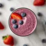 Close-up of a creamy strawberry blueberry smoothie, garnished with fresh berries on a marble surface.