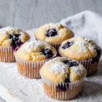 Five homemade lemon blueberry muffins on a white board, ready to be enjoyed.