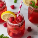 Fresh raspberry lemonade recipe served in three mason jars with raspberries, lemon, and mint.