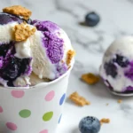 Homemade blueberry ice cream cheesecake scoops in a fun polka-dotted cup with fresh blueberries.