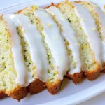 Four glazed slices of zucchini lemon bread healthy on a white platter, with lemon and zucchini beside it.