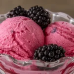 Two scoops of luscious raspberry ice cream in a glass bowl with fresh blackberries, ready to enjoy.