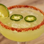 Vibrant close-up of a Spicy Jalapeño Margarita, rimmed with Tajín, garnished with lime and jalapeño slices.