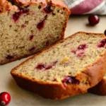 Golden-brown cranberry orange banana bread loaf with two slices, showing cranberries and moist texture.