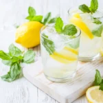 Two refreshing glasses of homemade mint lemonade with lemon slices and mint on a wooden board, highlighting the perfect recipe of mint lemonade.
