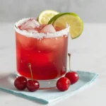 Top-down view of a fresh cherry margarita recipe with a salted rim, lime, and scattered cherries.