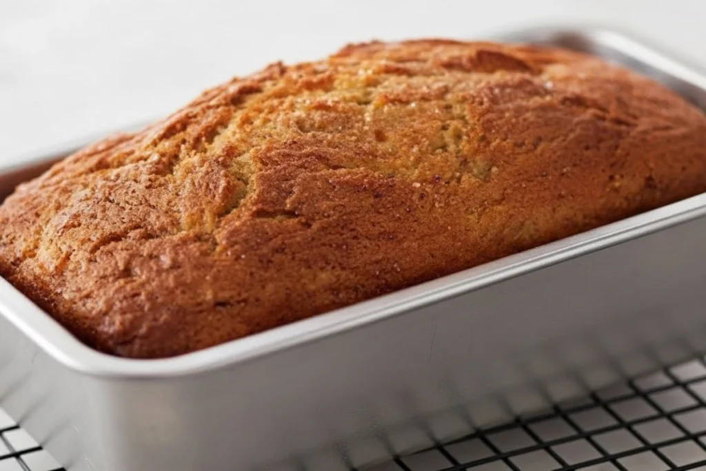 Freshly baked banana pineapple bread cooling in its loaf pan on a rack.
