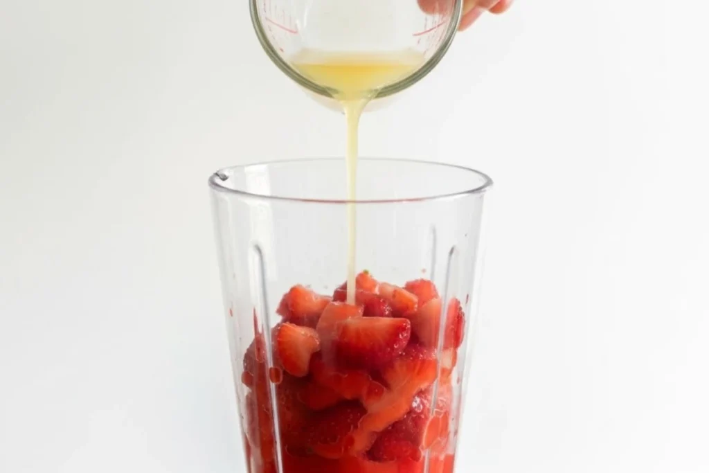 Hand pouring lime juice into a blender with strawberries, a key step in our strawberry margarita recipe.