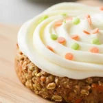 Delicious frosted carrot cake cookie with cream cheese and sprinkles on a wooden board.