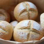 Baked German bread rolls in brown paper, cross-scored and dusted with flour, ready to enjoy.